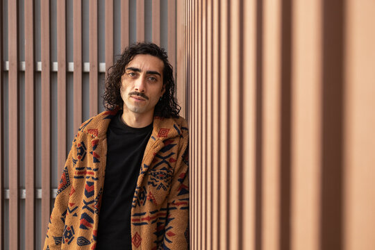 Man with Curly Hair and Patterned Jacket Leaning on Wall