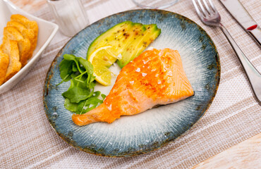 Baked salmon fillet served with fresh avocado and herbs on plate..
