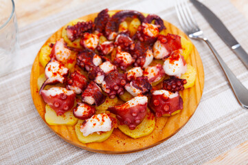 Appetizing chopped cooked octopus tentacles seasoned with smoked paprika with slices of boiled potato on wooden serving board. Traditional Spanish cuisine