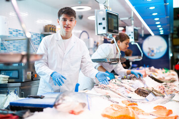 Positive young salesclerks in white work clothes posing in fish store with large stock