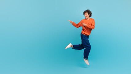 A young African American man with curly hair is playfully dancing against a vibrant blue background. His energetic movements express joy and enthusiasm, capturing a fun moment, copy space