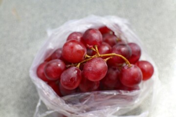 A plastic bag is filled with red grapes.