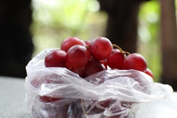 A plastic bag is filled with red grapes.