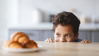 A cheerful boy peeks over the kitchen counter, eagerly eyeing some freshly baked pastries.