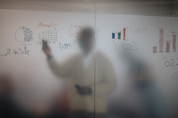 A diverse group of business people collaborate on sales strategies, using visual data on a glass board to analyze growth trends and market performance.