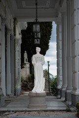 An antique statue made of white stone with a layer of old dirt stands among trees in a garden