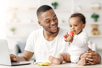 Young Black Daddy Working Online On Laptop And Playing With His Little Baby At Home, Happy African...