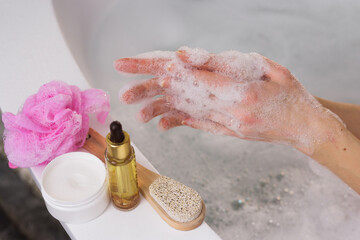 Woman applying shower gel on her hand in indoor bathroom, close-up on bathroom background, body and hair care products lying nearby