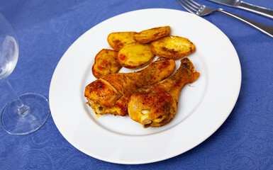 Delicious baked chicken legs with vegetable garnish of fried potatoes in skins served on plate..