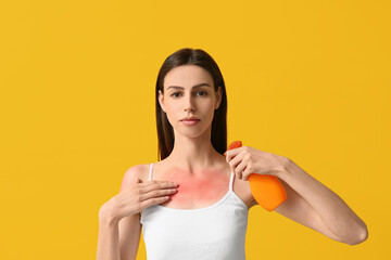 Young woman with red sunburned skin applying cream on yellow background