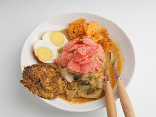 Homemade rice cake or Lontong Sayur, cooked with vegetable curry and served with boiled egg, fritter, and crackers on white plate