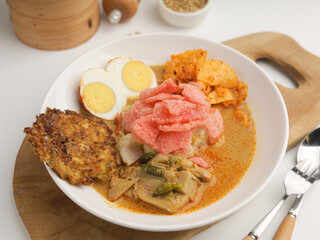 Homemade rice cake cooked with vegetable curry served with boiled egg, fritter, and crackers on white plate