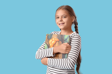 Cute schoolgirl with book on blue background