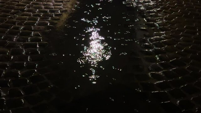 Reflection of light from a street lamp in a puddle of water during rain at night. A cobblestone street in the city.