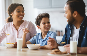 A joyful family shares a breakfast moment in their kitchen. The father talks with their son while the mother smiles, creating a warm atmosphere of love and connection.