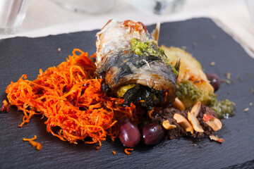 Grilled scomber fish roll with bacon served with vegetables on slate plate