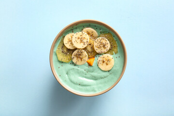 Bowl with tasty spirulina smoothie, banana, kiwi and chia seeds on blue background
