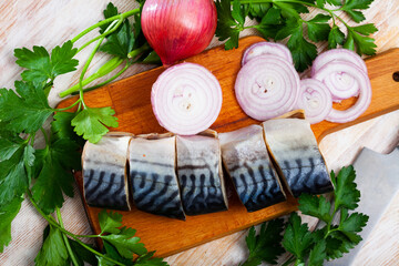 Pieces of delicious mild-cured scomber with fresh parsley and onion on wooden surface. Fish appetizer
