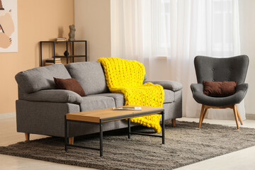 Modern interior of living room with stylish sofa, armchair and yellow knitted plaid