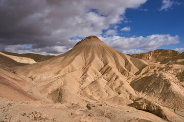 Majestic landscape of a remote mountain region in the Negev Desert. Close up view of orange sandstone hills and mountain folds. White clouds on blue sky.