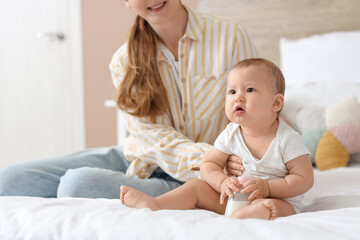 Mother feeding her little baby with milk from bottle in bedroom
