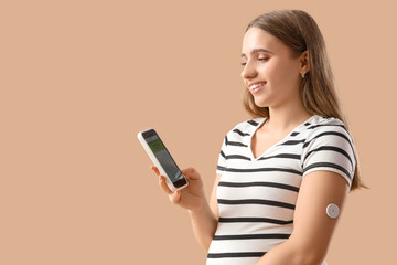 Young pregnant woman with gestational diabetes and glucose sensor using mobile phone for measuring of blood sugar level on beige background