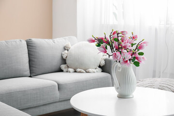 Vase with beautiful magnolia flowers on table near grey sofa in stylish living room