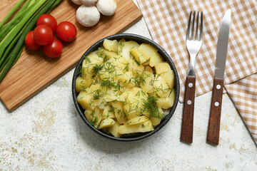 Bowl of tasty potato salad with ingredients and cutlery on light grunge background