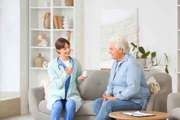 Obraz premium Female doctor giving pills to mature man on sofa at home