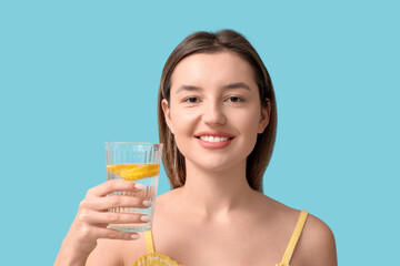 Beautiful young woman with glass of lemon infused water on blue background