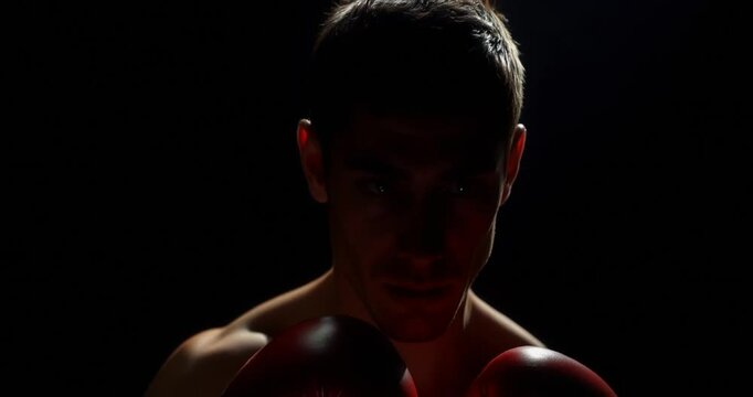 A high-angle perspective of a male boxer in training, with contrasting chiaroscuro lighting, deep shadows and the boxer appearing downcast.
