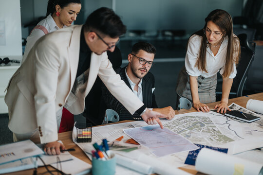 A project leader and team discuss an architectural design, examining maps and plans together in a modern office. Teamwork and collaboration drive their creative process.