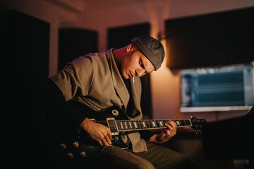 A focused musician plays an electric guitar. The dimly lit studio creates an intimate atmosphere,...