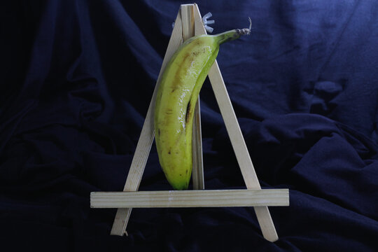 Banano sobre caballete de madera, con un fondo oscuro resaltando la frescura de la fruta.