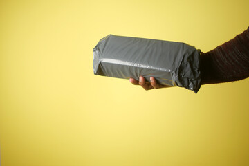 Hand Holding Wrapped Package Against Vibrant Yellow Background