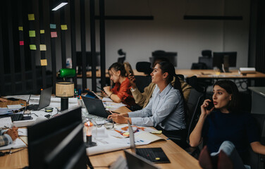 Multiracial colleagues engaged in a late-night brainstorming session, discussing projects and meeting deadlines in a modern workspace. Focused on strategic planning and analysis to achieve goals.