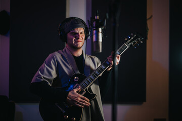 A guitarist deeply immersed in music, playing his electric guitar in a recording studio. The...