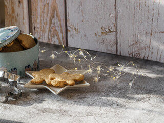 Box full of Christmas cookies next to a plate with cookies. Christmas lights. Christmas motifs.