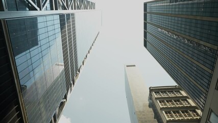 A dramatic upward view of towering skyscrapers in New York City. This image showcases the sleek, modern architectural lines and reflective glass surfaces of high-rise buildings against a clear sky.