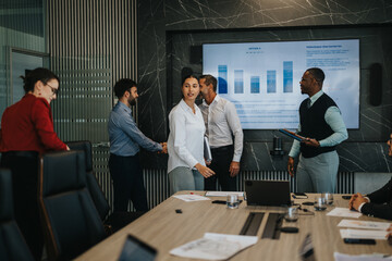 Multiracial business team engaged in a collaborative meeting. Professionals discuss ideas and strategies around a conference table with charts and graphs displayed on a large screen.