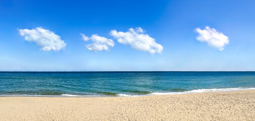 透き通った青い空にふわふわと浮かぶ雲と一面に広がる海と砂浜	