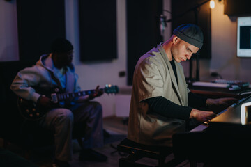 Two musicians intensely collaborate in a dimly lit recording studio, playing guitar and keyboard. Their focused expressions reflect creativity and passion, capturing the essence of music production