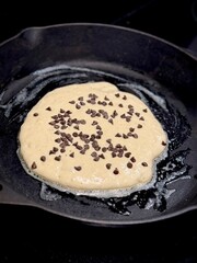 Close-up of chocolate chip pancake batter cooking in a cast iron skillet with melted butter.