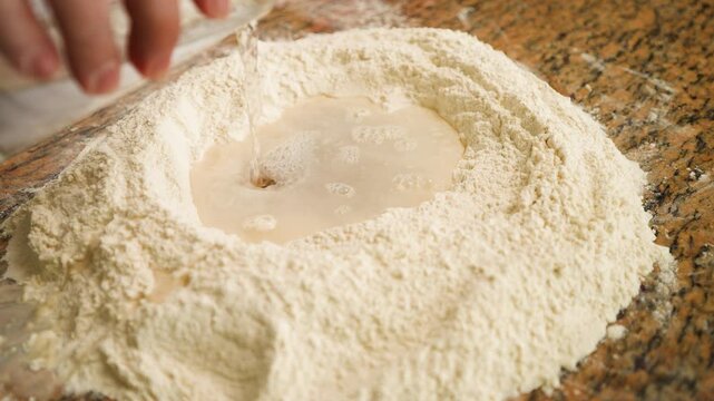 Captivating footage of water streaming into flour, signaling the beginning of a traditional pizza dough recipe