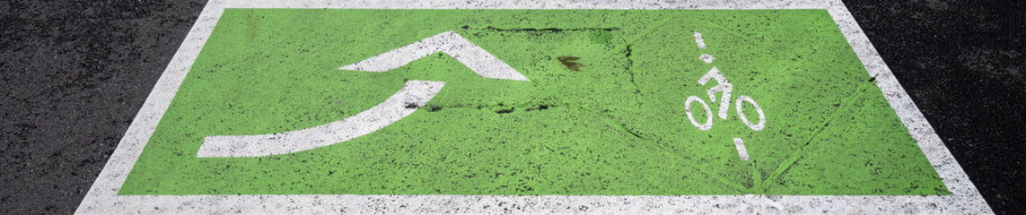 Traffic symbol markings on asphalt street, green bicycle lane with white bike symbol and left turn arrow, transportation background
