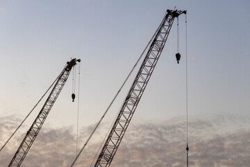 Dec 16 2024,Hong Kong.A series of construction cranes rise against a colorful sunset, casting long shadows over a busy construction site