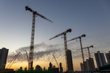 Dec 16 2024,Hong Kong.A series of construction cranes rise against a colorful sunset, casting long shadows over a busy construction site