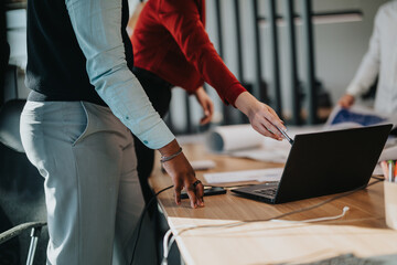 A group of business coworkers engaged in a brainstorming session at a busy office. Two team members are pointing at a laptop screen, discussing project details with focus and collaboration in action.