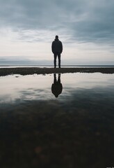 A man's reflection in water symbolizes self-reflection. A low-angle shot captures the vastness of his silhouette against an overcast sky