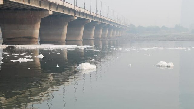 polluted river with industrial and domestic effluents toxic foam and concrete bridge at morning video is taken at yamuna river okhla barrage delhi india.